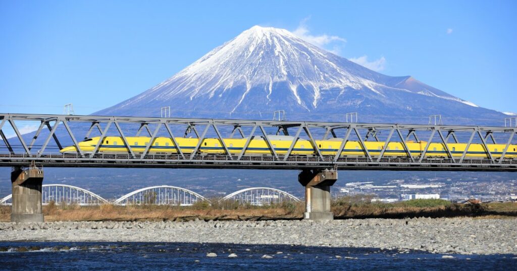 富士山を背景に黄色い新幹線が鉄橋を走る風景