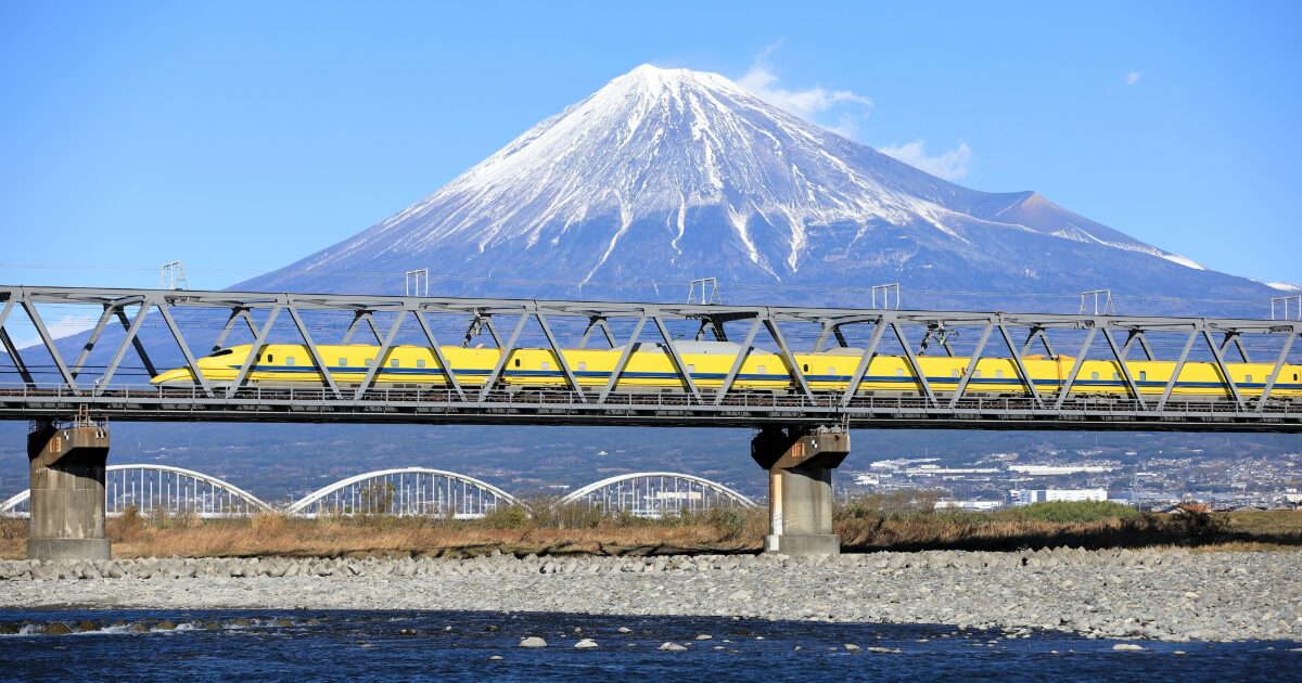 富士山を背景に黄色い新幹線が鉄橋を走る風景