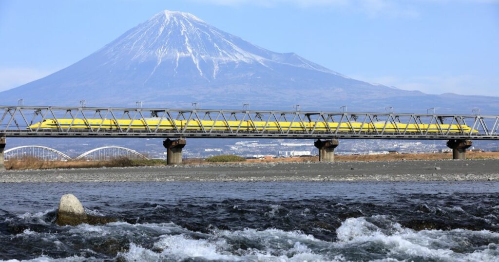 富士山と黄色い新幹線が鉄橋を走る風景