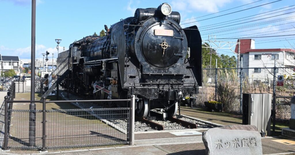 展示された黒い蒸気機関車と青空の駅前広場