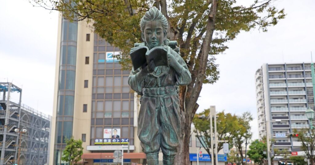 本を読む人物像の銅像と街中の景観
