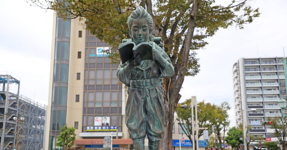 本を読む人物像の銅像と街中の景観