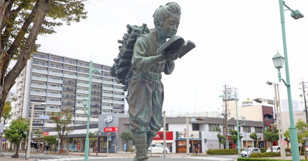 薪を背負い本を読む少年像と街中の風景
