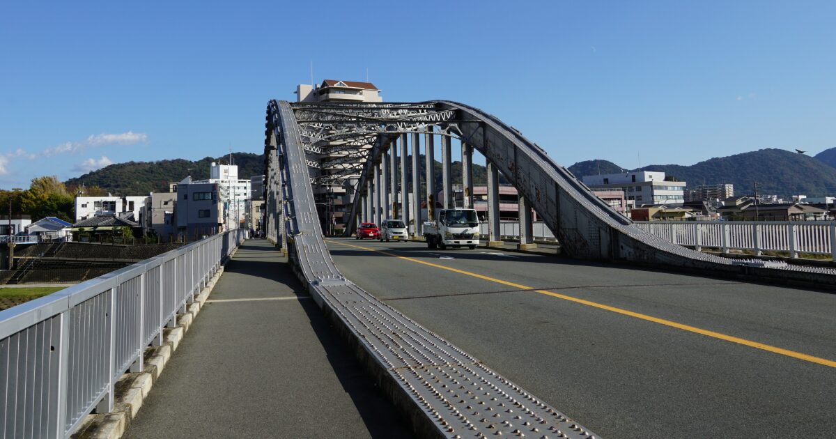 鋼鉄製アーチ橋を走る車と郊外の街並み