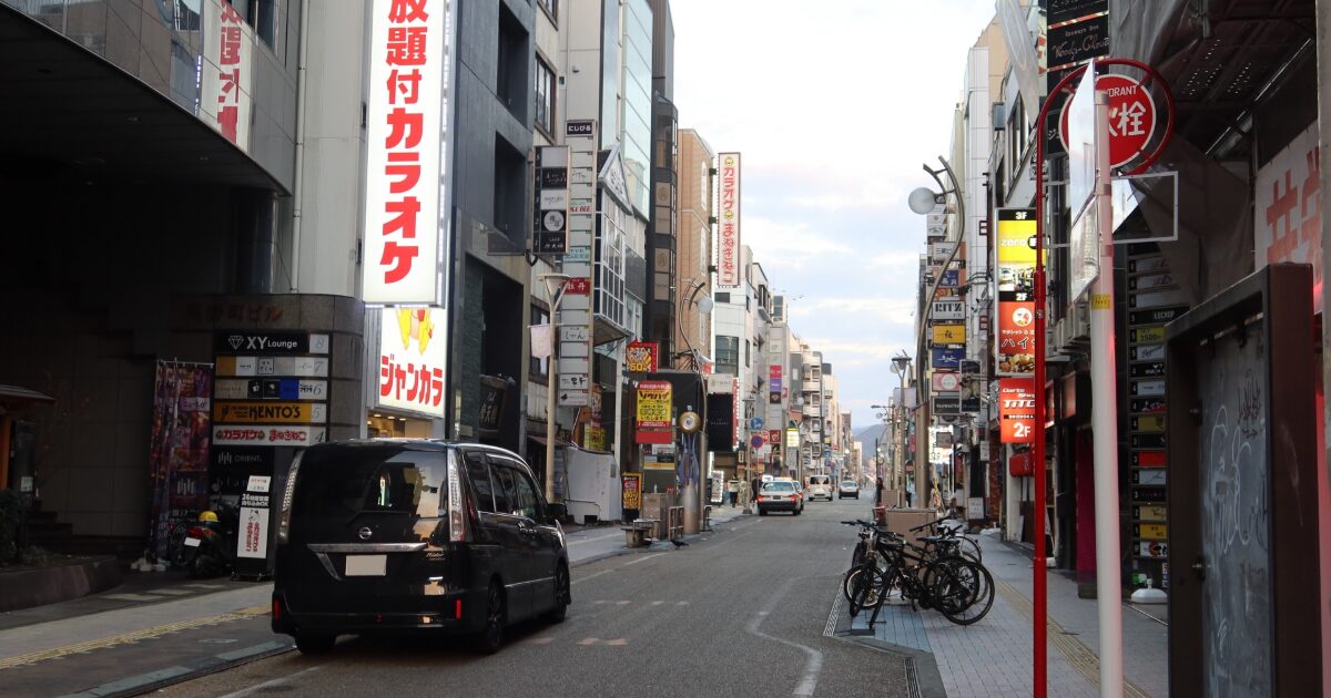 看板が並ぶ繁華街の通りと走行する車のある都市風景
